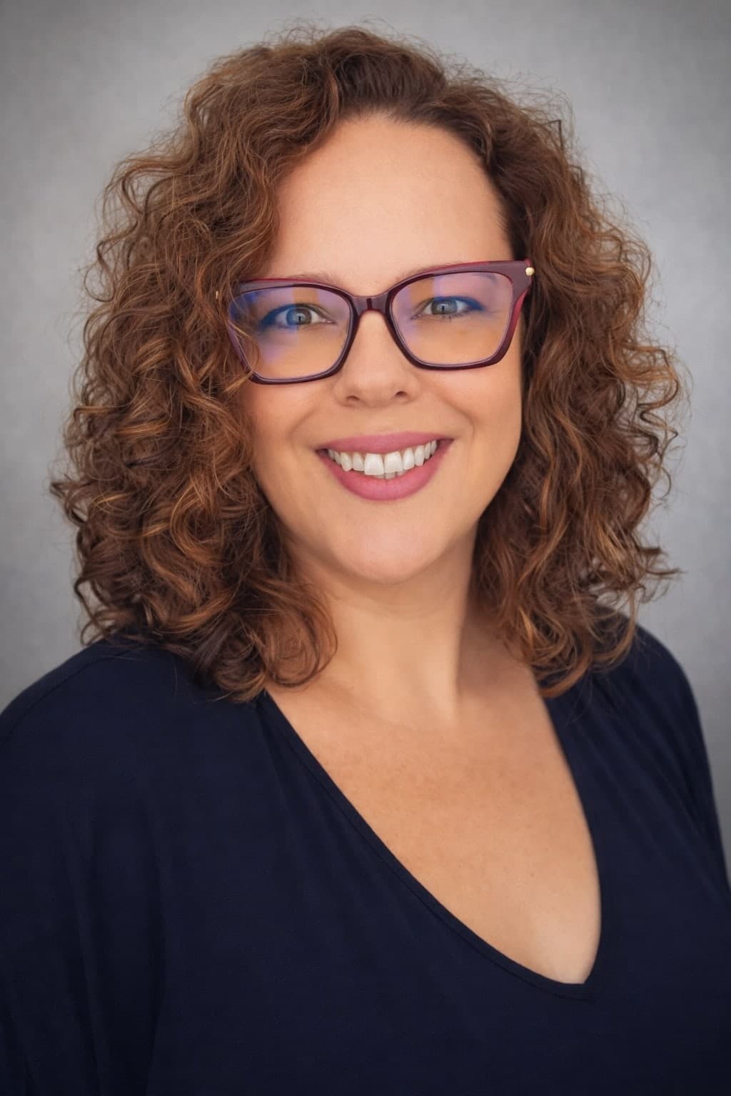 Retrato de Fabíola Aquino, de óculos, sorrindo, sobre fundo cinza